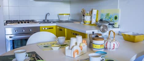 Una cocina moderna con armarios blancos, una estufa a gas y detalles en amarillo. Hay diversos utensilios de cocina y una tetera sobre la encimera.