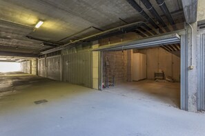 Eine große Garage im Industriedesign mit Betonböden und Metallwänden. Mehrere Garagentore, von denen einige geöffnet sind, geben den Blick auf eine Ziegelwand und eine Leiter frei.