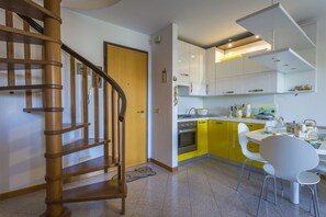 A kitchen with a wooden staircase, yellow cabinets, and white chairs.