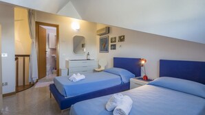 Een slaapkamer met twee bedden, een nachtkastje met lamp, een dressoir, een spiegel en een badkamer die door een open deur zichtbaar is.