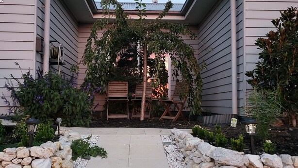 A pathway leading to a building with a covered entrance, stone walls, and a variety of plants. - Country Luxury. Delux Queen Bed, Full Bathroom. Private Unit. Massage chair. (Scarsdale)