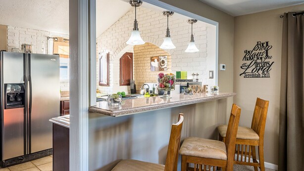 Une cuisine avec un mur en briques, un réfrigérateur en acier inoxydable, des chaises en bois et des luminaires suspendus.