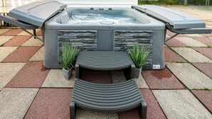 Un bain à remous avec un revêtement extérieur en pierre, deux marches menant à celui-ci, et deux plantes en pot placées de chaque côté.
