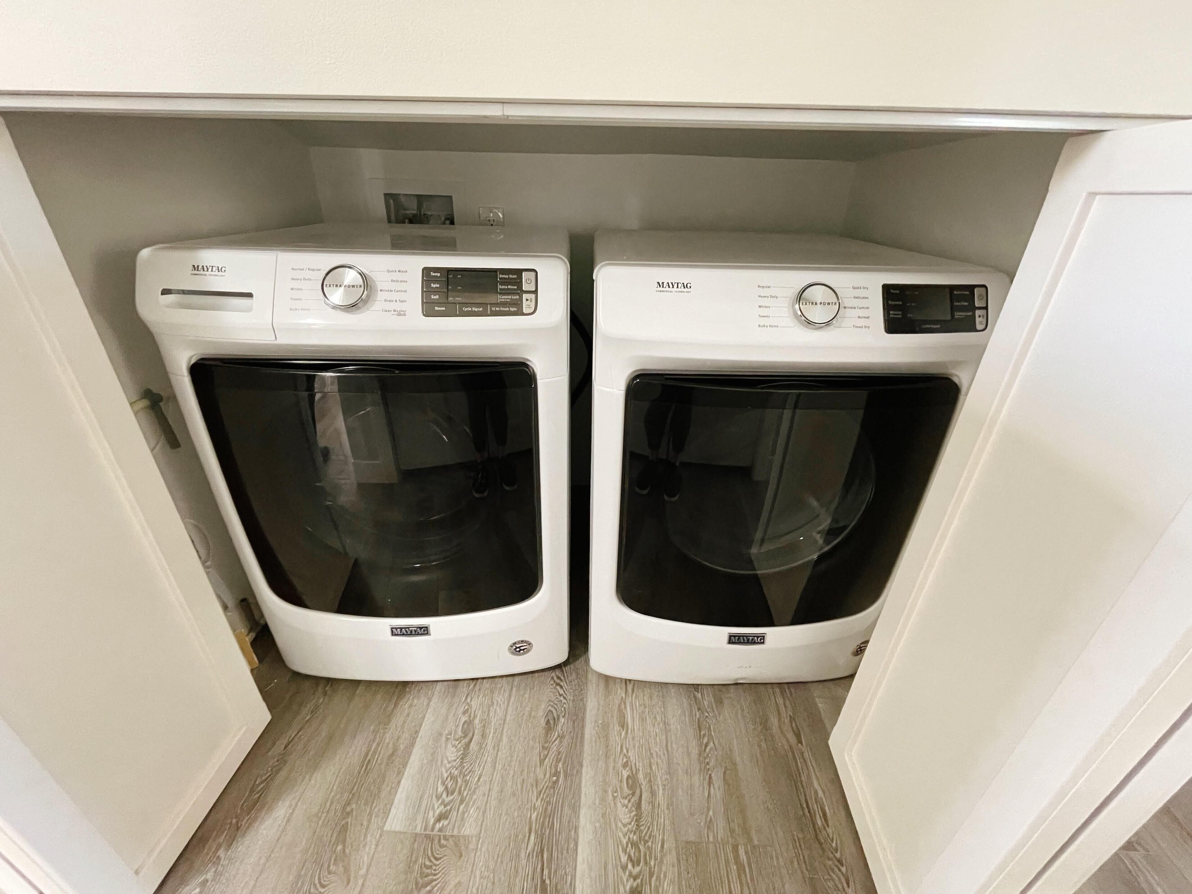 Ein Waschraum mit zwei Maytag Frontlader-Waschmaschinen unter einem weißen Schrank.