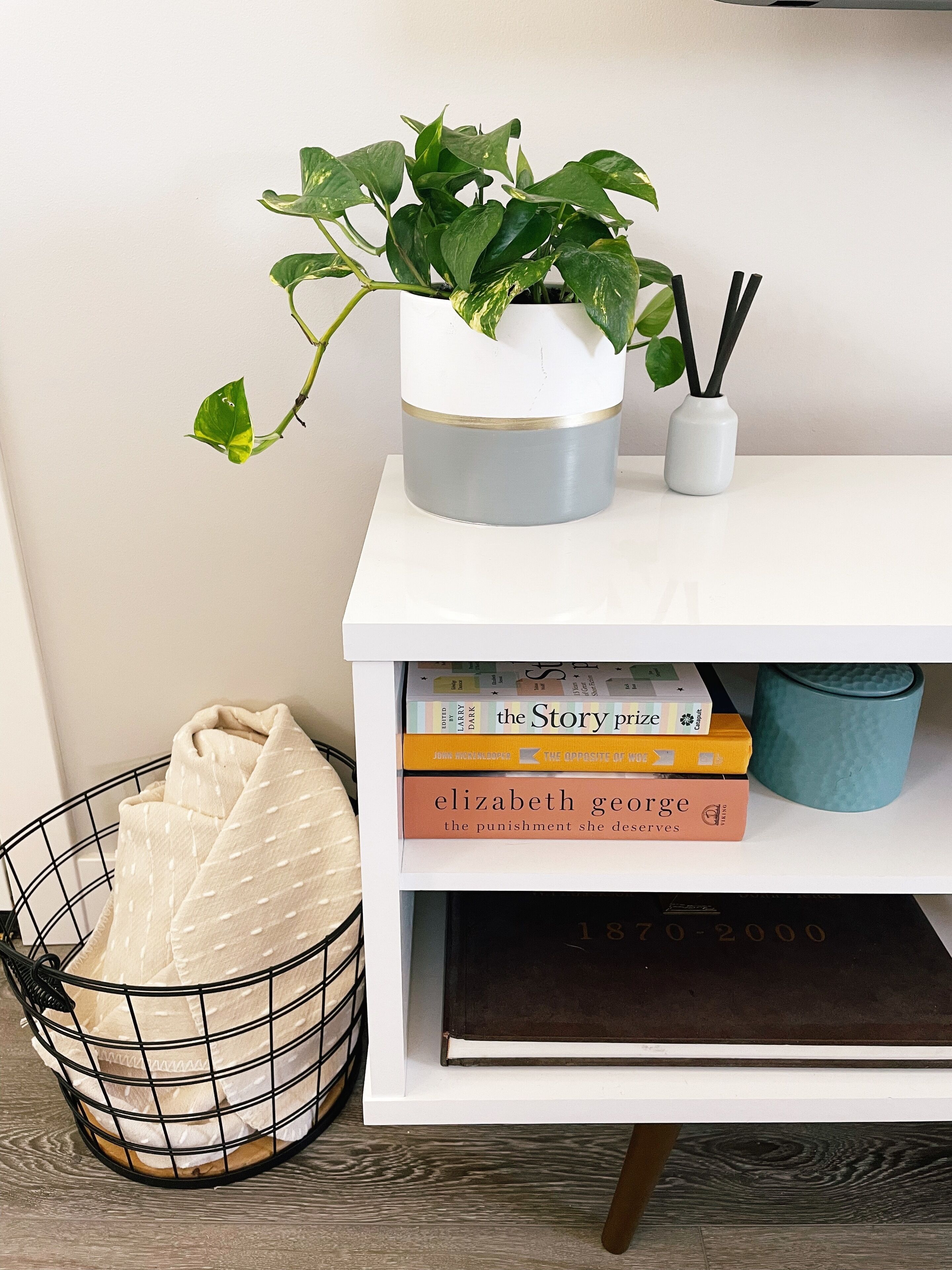A white shelf with a potted plant, a stack of books, and a blue mug.