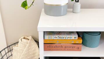 A white shelf with a potted plant, a stack of books, and a blue mug.