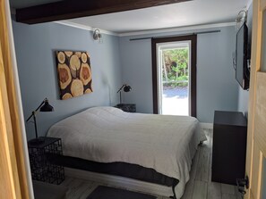 Una camera da letto con un letto, due comodini, una lampada a parete, un quadro e una finestra vista verde.