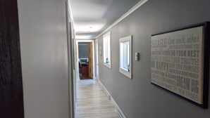 A hallway with a motivational quote on the wall, wooden flooring, and a door leading to a kitchen area. - Chalet lacbrome (Knowlton)
