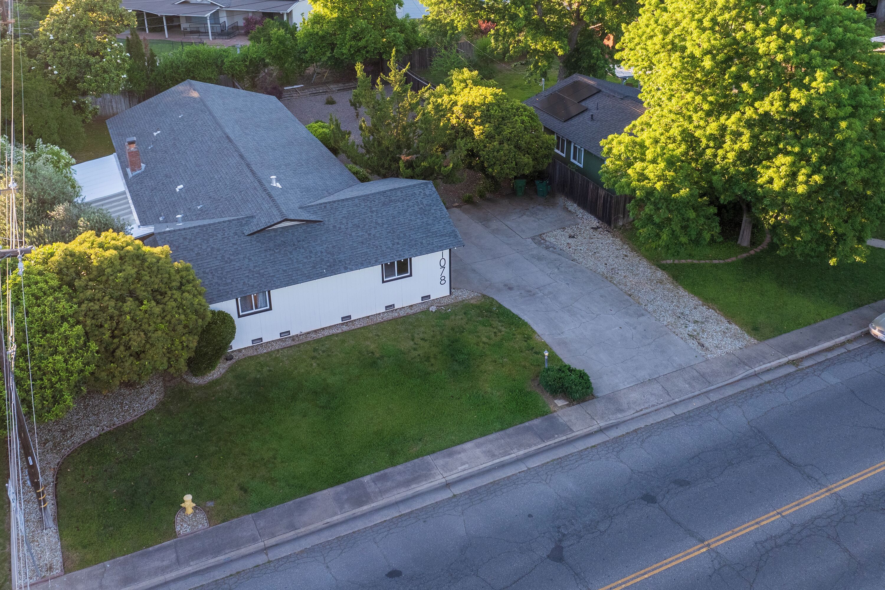 An aerial view of a residential area with a house, a driveway, and surrounding greenery.