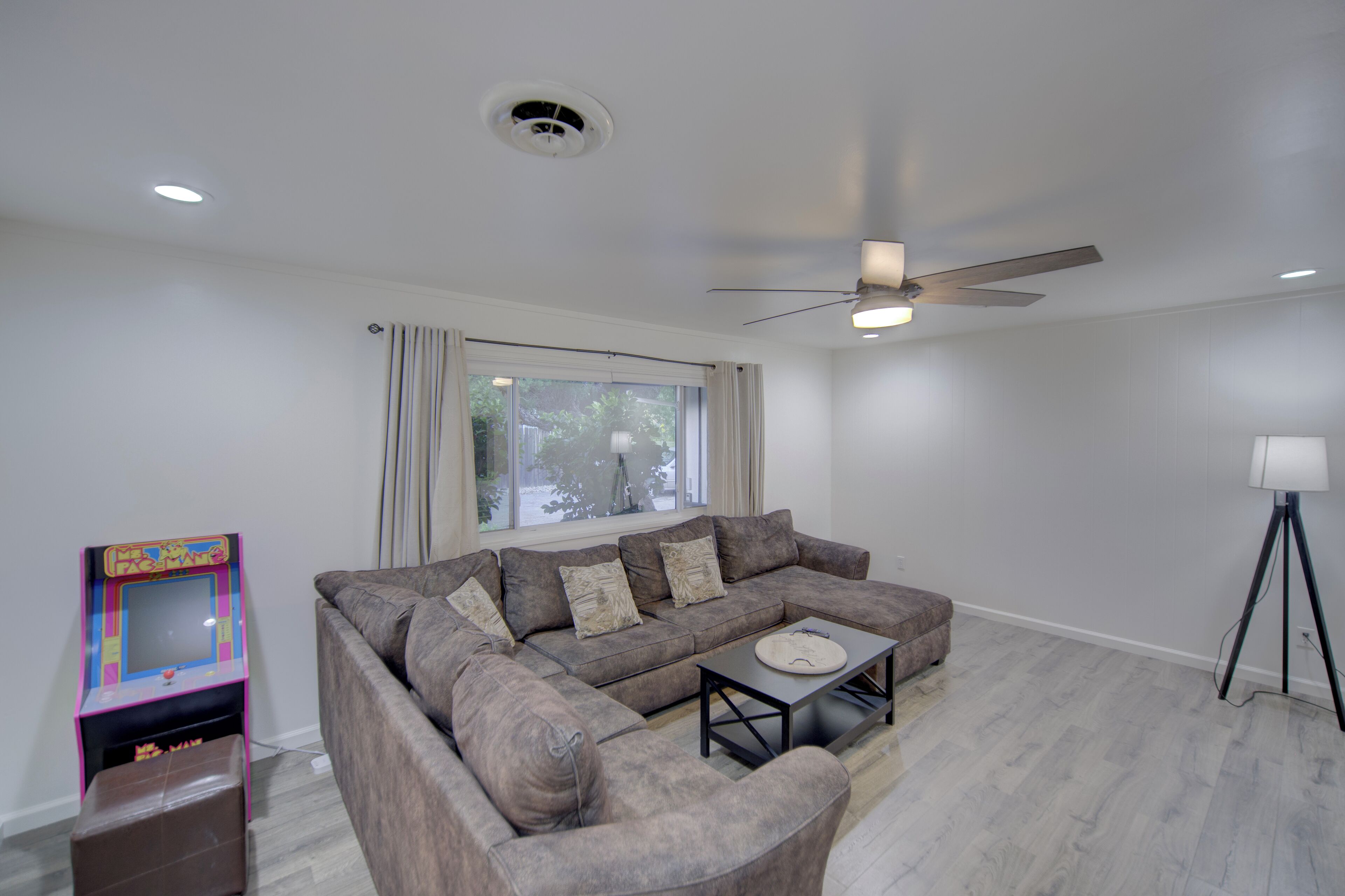 A modern living room with a sectional sofa, a coffee table, a ceiling fan, and a window with curtains.