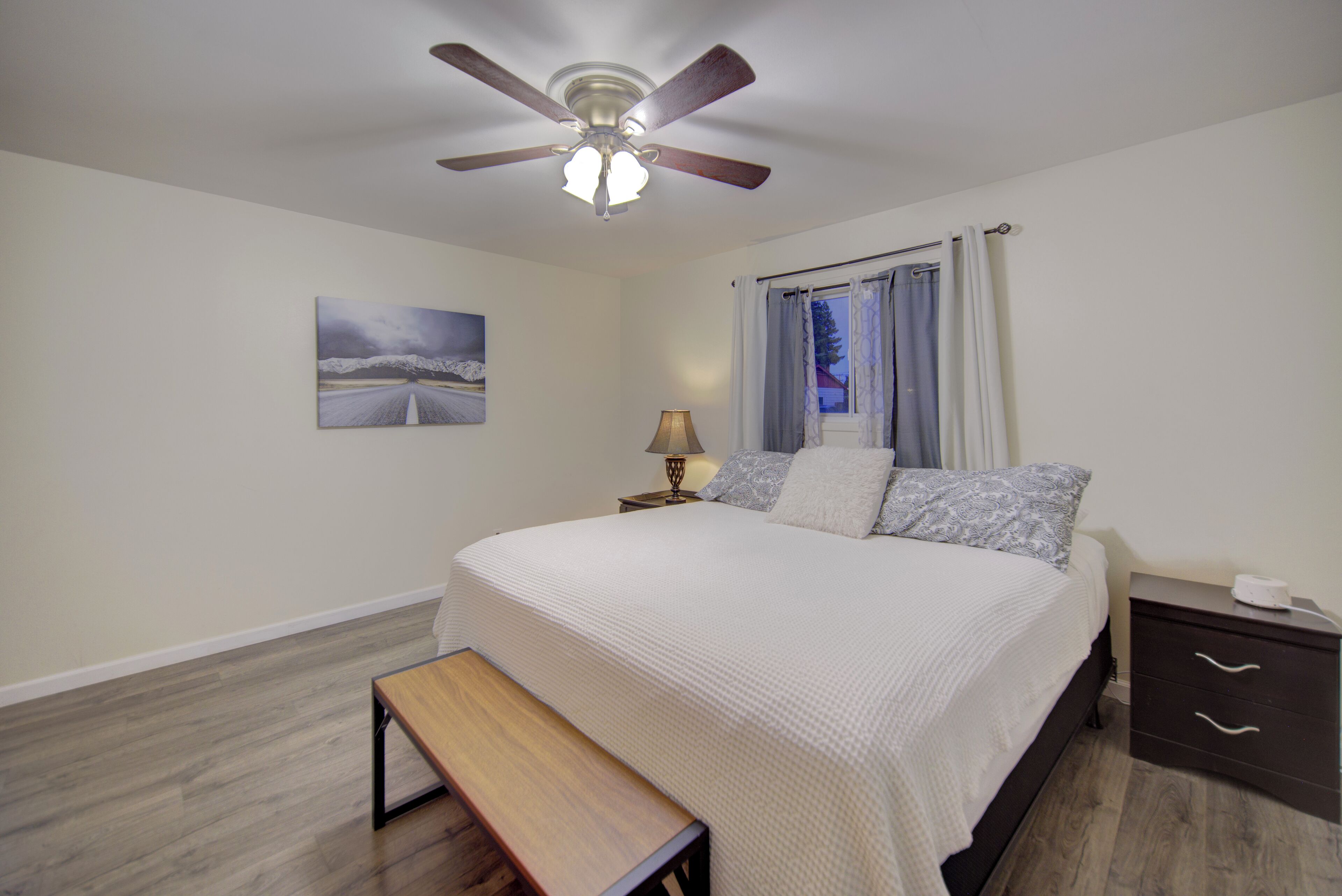 Une chambre à coucher comprenant un lit, un ventilateur de plafond, une table de chevet avec une lampe, un banc et une commode.