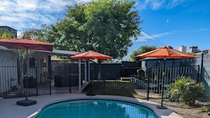 A swimming pool with a curved edge, surrounded by a black metal fence, and two red umbrellas providing shade. - An oasis featuring a pool, where quiet luxury meets backyard tranquility. (Peoria)