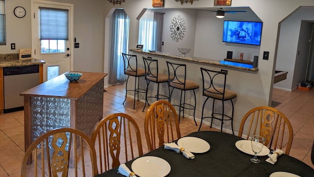 A modern kitchen with a bar area, dining chairs, and a TV mounted on the wall. - An oasis featuring a pool, where quiet luxury meets backyard tranquility. (Peoria)