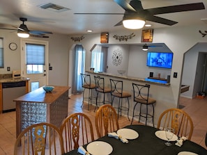 A modern kitchen with a bar area, dining chairs, and a TV mounted on the wall. - An oasis featuring a pool, where quiet luxury meets backyard tranquility. (Peoria)