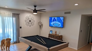 A pool table in a room with a ceiling fan, a TV mounted on the wall, and a decorative wall piece. - An oasis featuring a pool, where quiet luxury meets backyard tranquility. (Peoria)