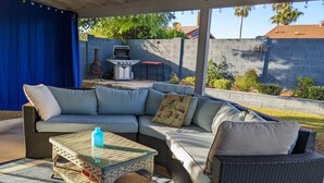 A covered patio area with a wicker sofa, a glass coffee table, and a grill. - An oasis featuring a pool, where quiet luxury meets backyard tranquility. (Peoria)