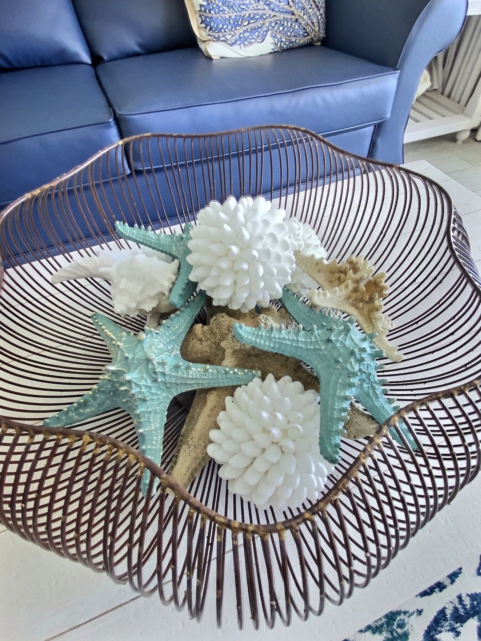 A round metal coffee table with a white and blue patterned base, decorated with white flowers and a turquoise starfish.