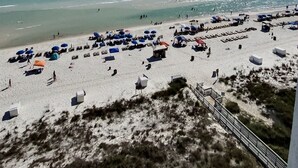 Ein Strand mit Sonnenschirmen und Liegestühlen, einem klaren Himmel und dem Meer.