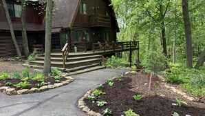 Une cabane en rondins dotée d’une terrasse en bois et d’un chemin de pierre menant à l’entrée.