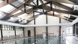 Une piscine intérieure avec des couloirs bien délimités, un plafond haut orné de poutres en bois et un sol carrelé.