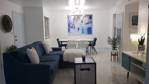 Un salon moderne avec un canapé bleu, une table à manger avec des chaises, un meuble blanc et une plante décorative.
