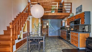 Una cocina amplia con armarios de madera, un comedor con mesa y sillas, y una escalera con barandilla de madera.
