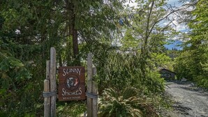 Un letrero de madera anuncia Sunny Shores Beach House, rodeado de vegetación densa.
