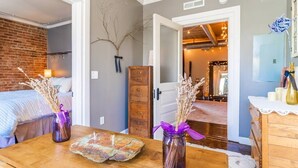A cozy room with a bed, a wooden table with a vase and a rustic plate, and a door leading to another room with a chandelier. - Historic Loft in Heart of St Elmo ★ Staycation Gem (Chattanooga)