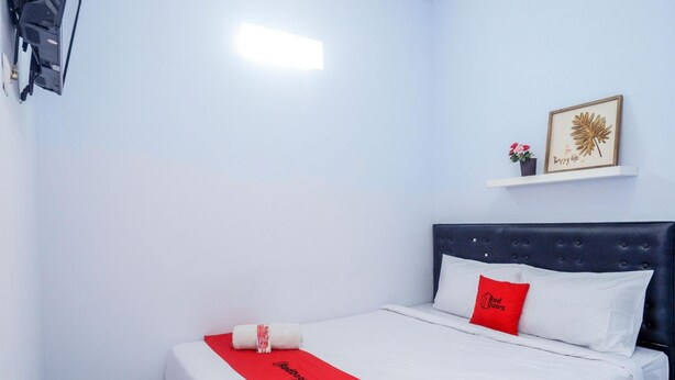 A neatly made bed with white and red bedding, a red pillow, and a red towel on a white bedspread. - OYO 3170 Songo Residence (Semarang)