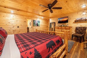 Een houten kamer met een bed, een plafondventilator, een televisie en een open haard.