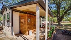 A covered porch with a wooden cabin, a tree, and a fire pit.