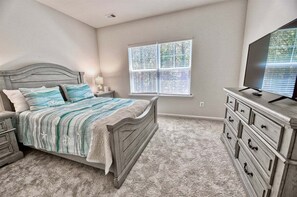 Une chambre à coucher avec un lit, une commode, un téléviseur et une fenêtre avec des stores.