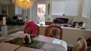 Un espace repas comprenant une table en verre, des chaises, un lustre et une vue sur l’extérieur grâce à de grandes fenêtres.