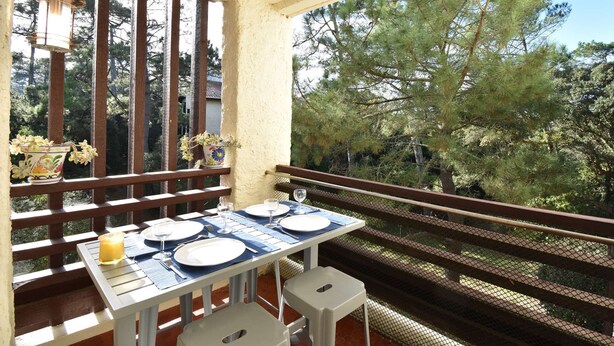 A balcony with a table set for two, overlooking a forested area. - Seignosse “LE PIGNADA” Apartment for 4 people. (SEIGNOSSE)