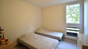 A small, bright room with two single beds, a window with a view of trees, and a wooden toy shelf. - Seignosse “LE PIGNADA” Apartment for 4 people. (SEIGNOSSE)