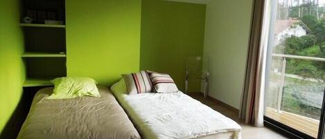 A bedroom with two beds, a green wall, and a large window with a view of trees.