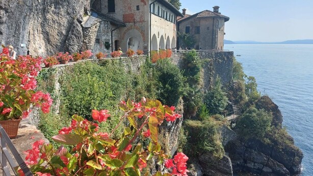 A historic building with arched windows and a stone facade, situated on a cliff overlooking a body of water.
