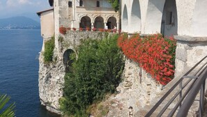 A historic building with a stone facade, arched windows, and a balcony with red flowers.