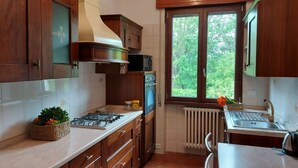 A kitchen with wooden cabinets, a gas stove, a microwave, and a window with a view of greenery.