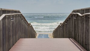Een houten looppad dat naar het strand leidt, met golven op de achtergrond.