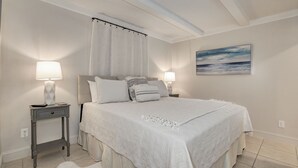 Een slaapkamer met een groot bed, twee nachtkastjes met lampen, een hoofdeinde, een raam met gordijnen en een schilderij aan de muur.