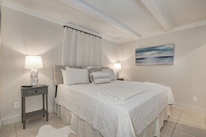 Ein Schlafzimmer mit einem großen Bett, zwei Nachttischen inklusive Lampen, einer Kopfteil, einem Fenster mit Vorhängen und einem Bild an der Wand.