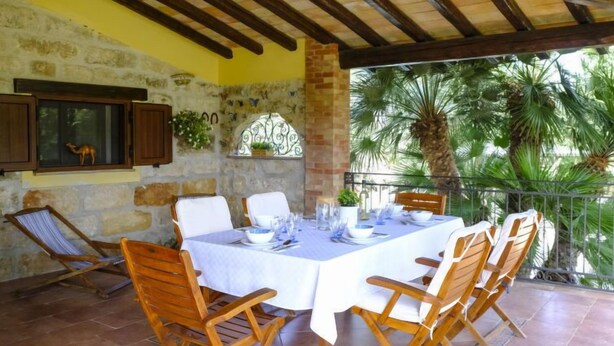 An outdoor patio with a stone wall, wooden ceiling beams, and a table set for dining.