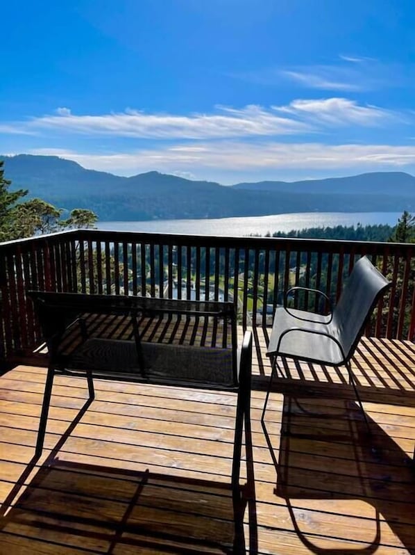 A wooden deck with two chairs and a table, overlooking a lake and mountains.