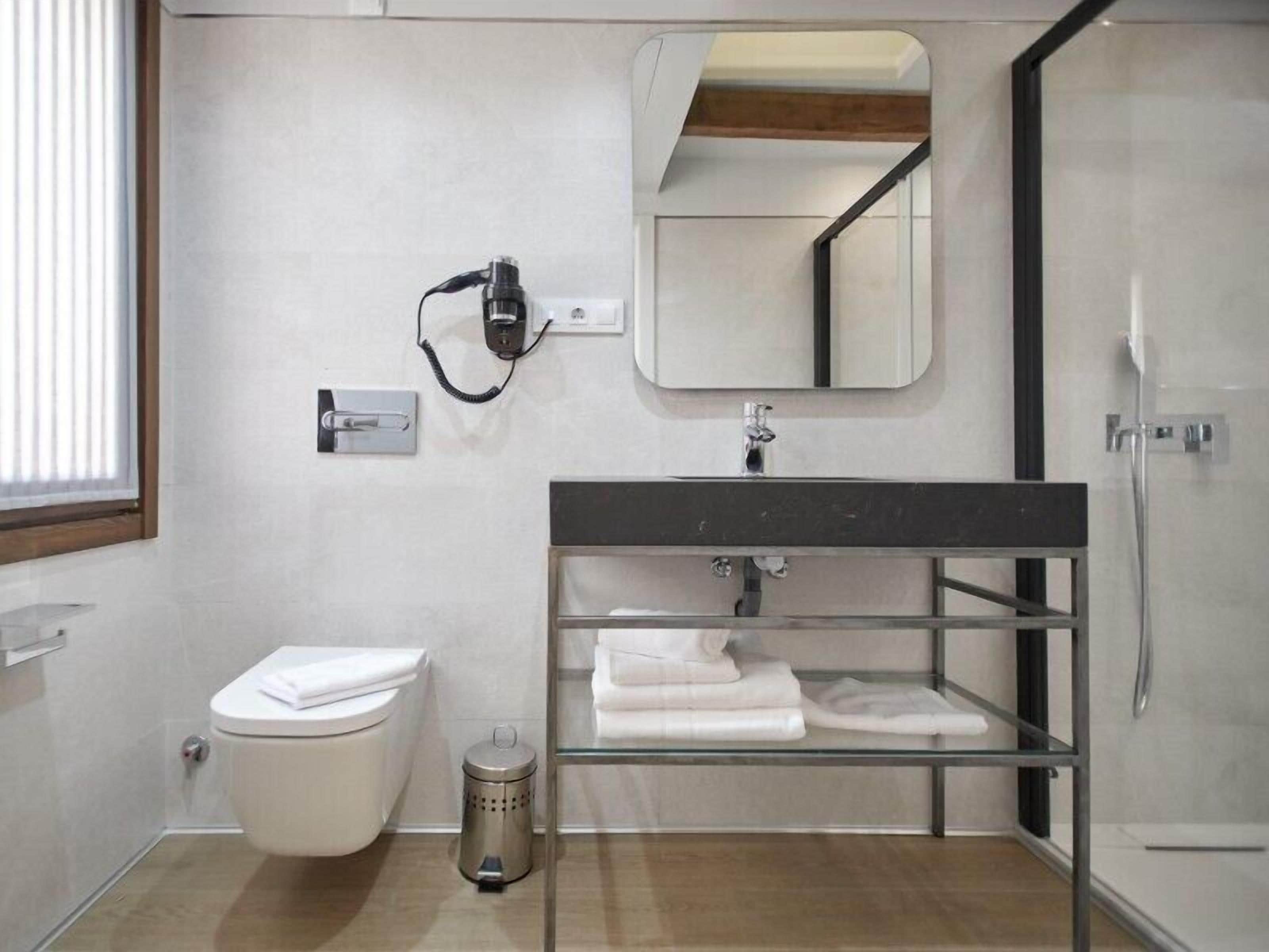 Une salle de bain moderne comprenant des toilettes, un lavabo en verre avec un cadre en métal, un miroir et une douche.