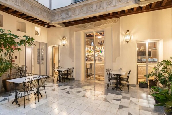 A spacious indoor area with tiled flooring, multiple tables and chairs, and decorative wall sconces.
