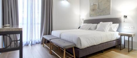 Un dormitorio con cama, banco, mesita de noche y un cuadro en la pared.
