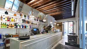 Een bar met een lange toonbank, planken met flessen en hangende lampen.