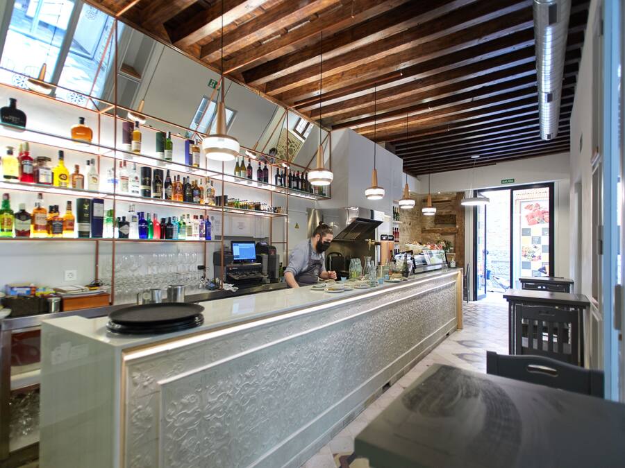 A bar with a long counter, shelves with bottles, and hanging lights.