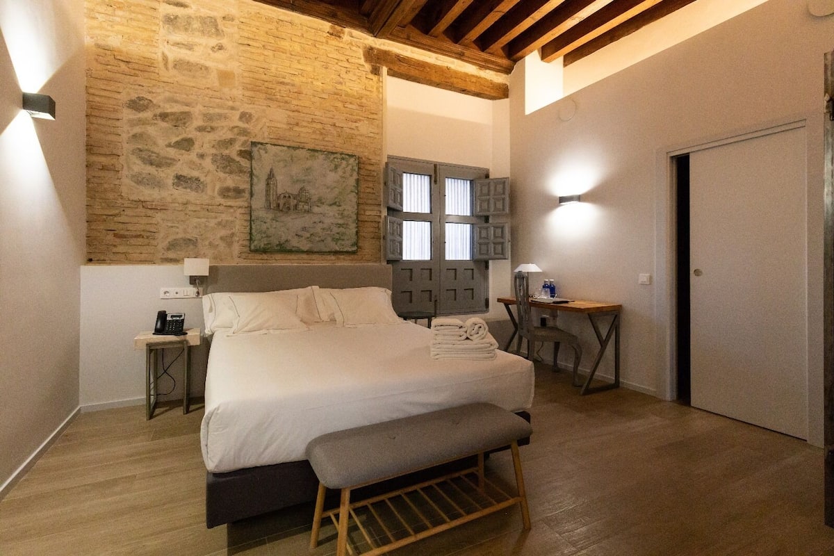 Une chambre à coucher comprenant un lit, un bureau, une chaise, un banc, un téléphone et un tableau accroché au mur.